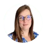 Een vrouw met lang bruin haar en een ronde bril, gekleed in een blauwe top met een wit bloemenpatroon, glimlacht lichtjes tegen een witte achtergrond.
