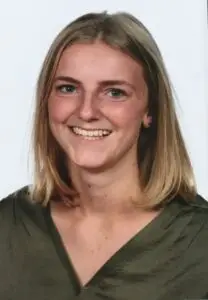 Een jonge vrouw met steil, schouderlang blond haar glimlacht naar de camera. Ze draagt een groene top en staat te poseren tegen een effen witte achtergrond.