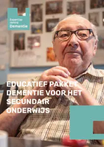 Een oudere man met een bril en een gestreept shirt zit aan een tafel, met zijn handen gevouwen. De tekst luidt: Educatief pakket dementie voor het voortgezet onderwijs. Aan de muren hangen familiefoto’s.