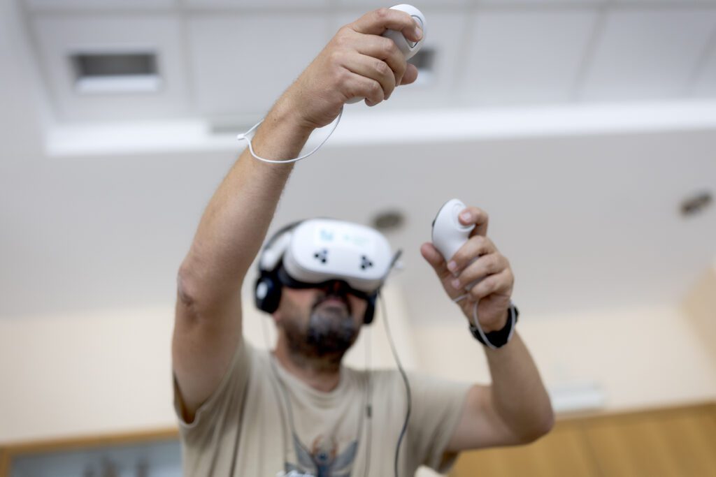 Iemand die een virtual reality-headset en een koptelefoon draagt, houdt twee bewegingscontrollers vast en beleeft binnenshuis een VR-ervaring.