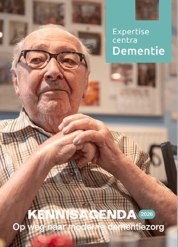 Een oudere man met een bril zit aan een tafel met zijn handen gevouwen. De tekst luidt: Expertisecentra Dementie en KENNISAGENDA 2026 – Op weg naar moderne dementiezorg...